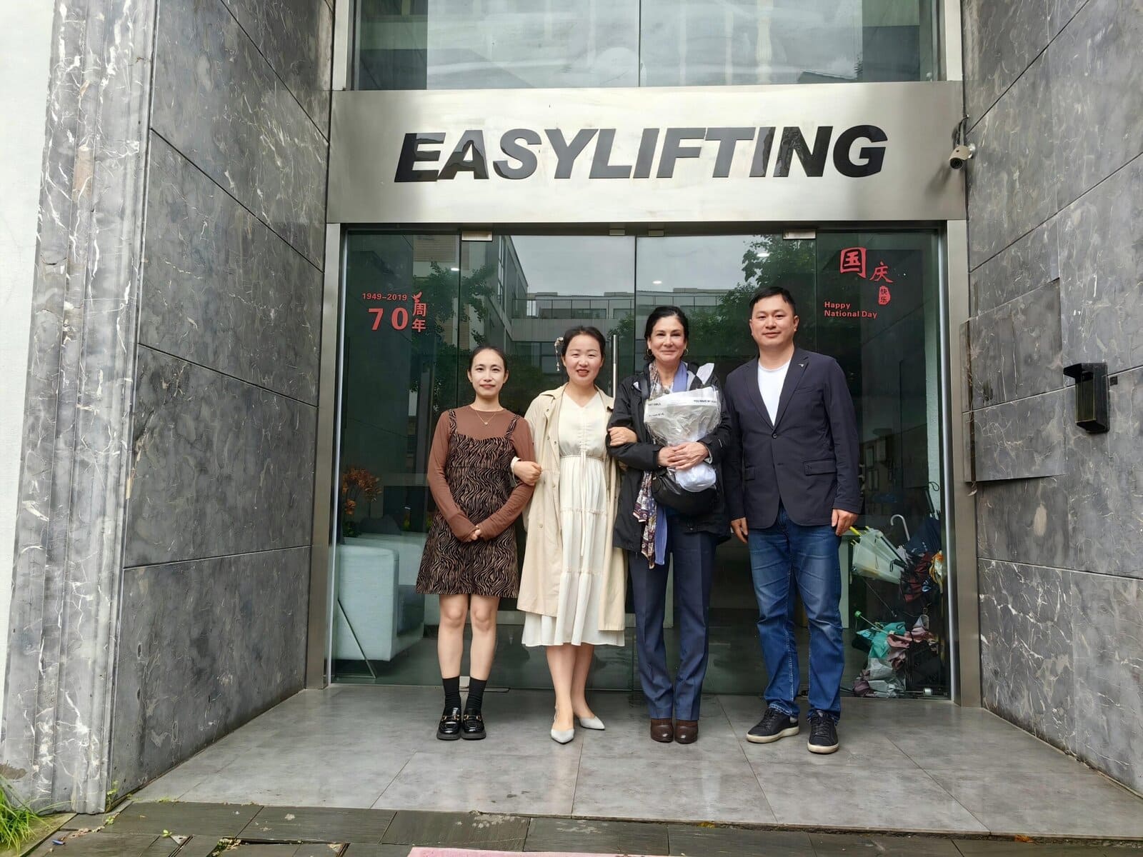 Group of four professionals standing in front of EASYLIFTING office entrance, smiling and dressed in business casual attire, representing a team in the fitness and lifting industry.